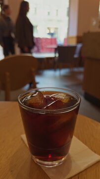 Cafe table with iced beverage and city view. Streetside cafe setting with cold drink and bustling background. Refreshing iced coffee on city sidewalk table with lively pedestrians and window scenery