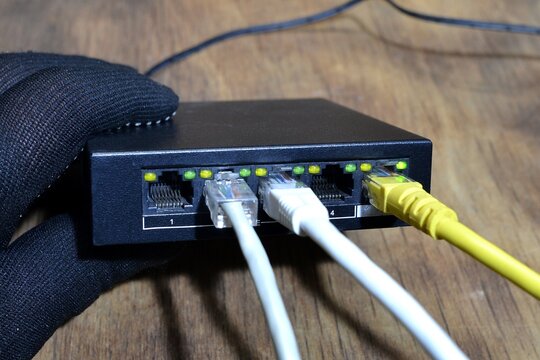 Ethernet switch,network device with five ports,three of them connected with Ethernet cables.A hand wearing a black glove.