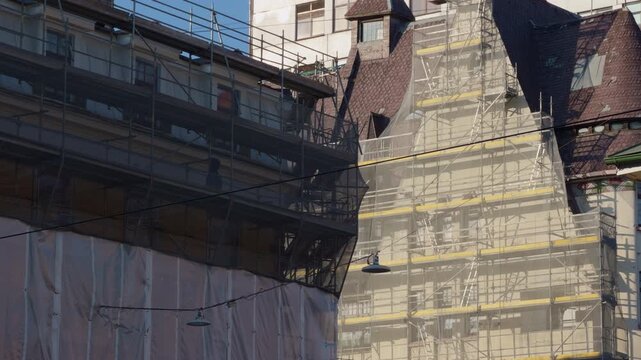 Ancient roof preservation. Construction environment highlights detailed work on old building features. Architectural conservation effort captures layered turrets and steep gables under protection