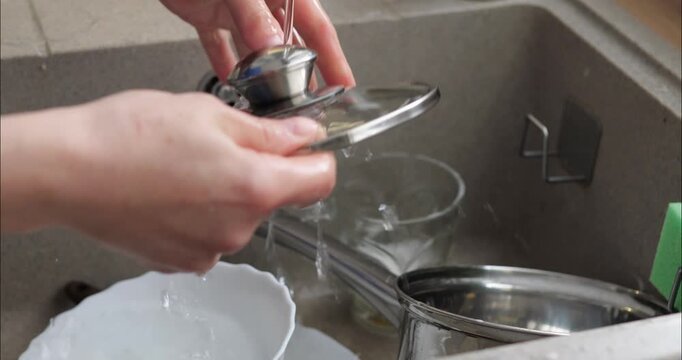 Housewife washing dishes by hand. Dirty dishes stand in the kitchen sink soaking wet. Plates and pots after dinner.