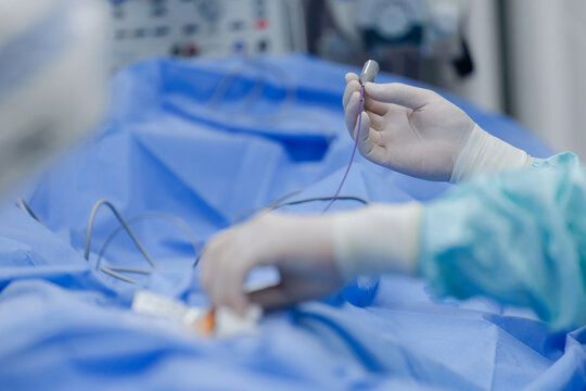 Surgeon handling catheter during cardiac catheterization procedure in operating room with gloved hands for surgical intervention and clinical treatment background
