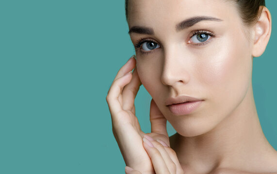 Beautiful young women with perfect fresh skin and makeup touches her face. Portrait of model with make-up, eyebrows  and long eyelashes. Beauty and Spa, skincare and wellness. Selective focus.