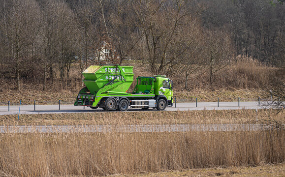 Kungsbacka, Sweden - March 20 2026: Bright green skip loader truck driving beside rural reeds and woodland.