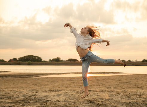 Beautiful little girl jumps on the sand on the river bank. Little ballerina girl is dancing on the nature. Kid and child on vacation. Selective focus