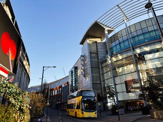Busy shopping street in Manchester UK with yellow double decker bus outside Next store and modern glass mall