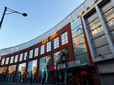 Roxy Ballroom venue facade in Manchester, UK with curved red brick and glass frontage reflecting city streets and evening light
