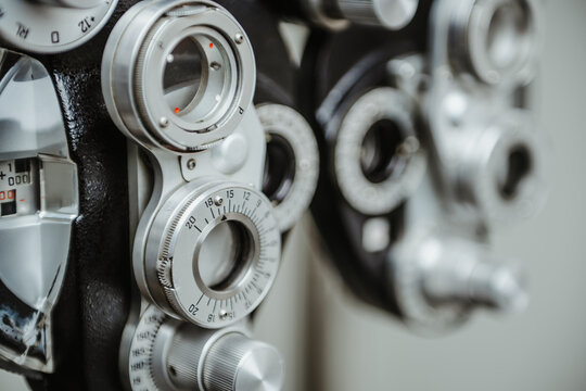 Phoropter close up vision testing equipment in eye clinic. Close-up of an ophthalmic phoropter with metal dials and adjustment knobs for vision testing in a medical setting.
