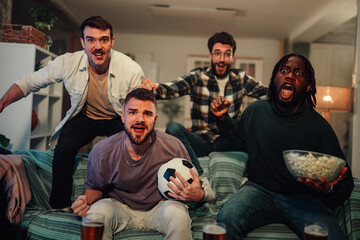 Diverse friends cheering loudly while watching an exciting soccer game on television at home, celebrating a goal or victory © Zamrznuti tonovi