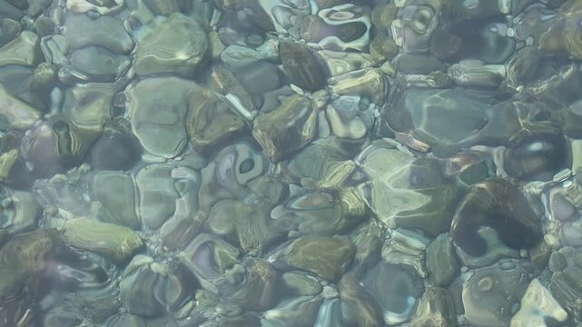 A close-up of the actually splashing clear turquoise water with underwater rocks on the bottom.