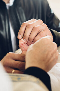 Adult hands gently holding baby foot during ceremony