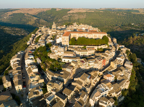 Aerial view of the historic stone buildings of Ragusa Ibla featuring the San Giorgio Cathedral dome and lush green valleys in Ragusa, Sicily, Italy.