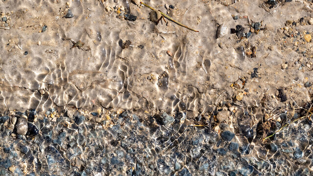 Sunlight reflections on shallow water over sand and gravel creating natural abstract texture with ripples and transparency, Cotignac, Provence, France