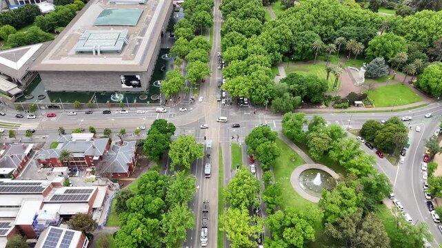 Dynamic drone footage starting with top down vertical aerial view over tree lined streets and tram lines, rising to reveal Melbourne skyline, city center and urban landscape in Melbourne, Australia.
