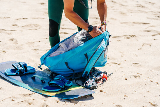Person preparing kitesurfing equipment on beach sand