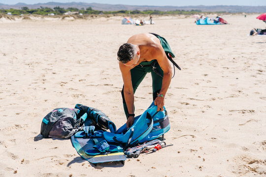 Person preparing kitesurfing equipment on beach for water sport