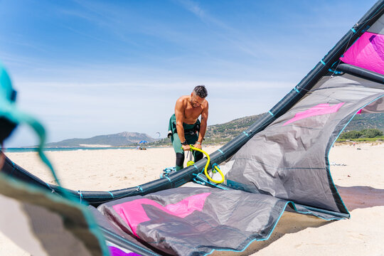 Person inflating kite for kitesurfing on beach