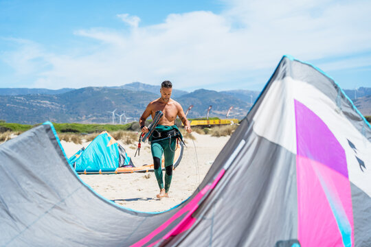 Person preparing kitesurfing equipment on a sandy beach