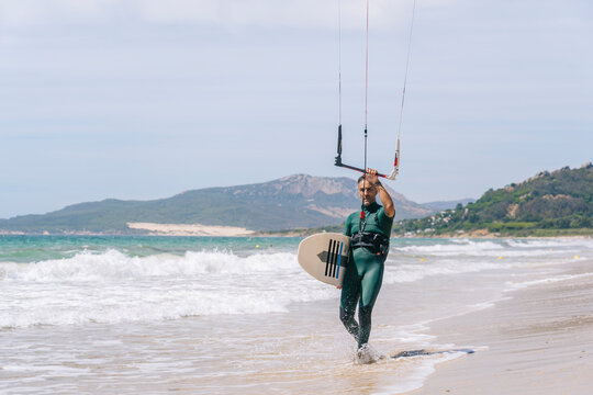 Kitesurfer carrying board and kite bar on beach