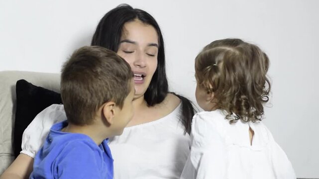 Latina mom talks and laughs a lot with her two children on the sofa, affectionate hug and family connection at home now.