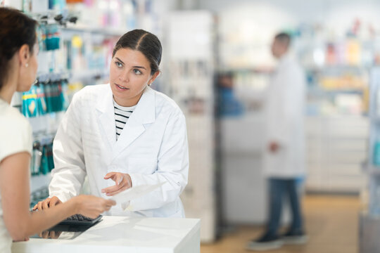 Polite young female pharmacist consulting woman client about medicine indicated in her recipe in chemist's shop