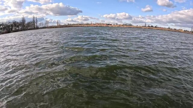 rhythmic waves in the clear water of the lake, blue sky with white glazes, bare trees on the opposite bank