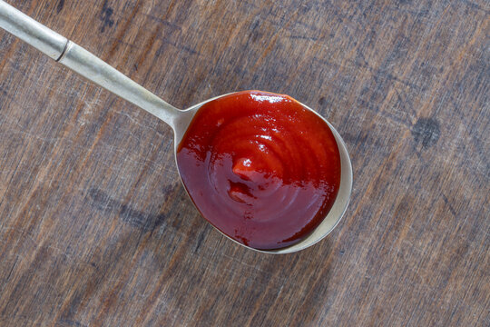 Red tomato ketchup or BBQ sauce in spoon on rustic wood. Closeup of thick red sauce in a metal spoon over weathered wooden background. Perfect for culinary concepts food blogging and restaurant menus