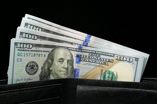 A black leather wallet filled with a stack of new hundred-dollar bills, showcasing financial security