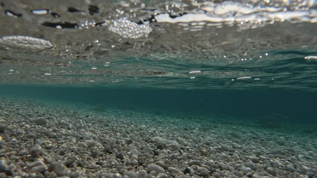 Crystal-clear water gently lapping pebble beach in greece. Sunlight glistens on the surface of calm, transparent water as gentle waves wash over a smooth pebble beach, revealing the seabed below