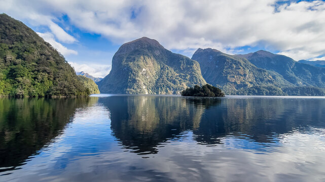 Reflections of the towering mountains and cliffs at Doubtful Sound on a blue sky sunny day
