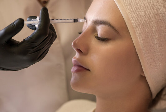 Hands of cosmetologist making injection in face, lips. Young woman gets beauty facial injections in salon. Face aging, rejuvenation and hydration procedures. Close up. Selective focus.