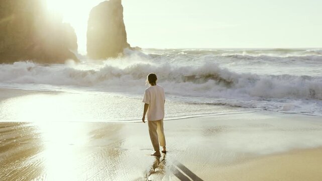A carefree woman in casual clothing enjoying sunset, walks and splashes in the ocean surf during sunset at "Praia da Ursa" beach, near Sintra, Lisbon, Portugal. Stock slow motion video