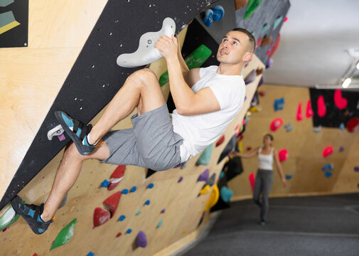 Male visitor to fitness club clambs wall for amateur climbers, side view. Active recreation, hobbies, recreation for active and sporty people