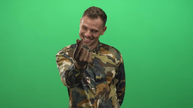 Man soldier in camouflage shirt beckons with fingers showing hand to camera in studio; playful invitation.
