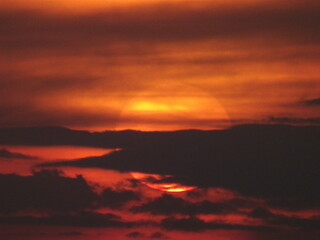 Obraz premium Dark dramatic sunset with sun hidden behind clouds intense sky background