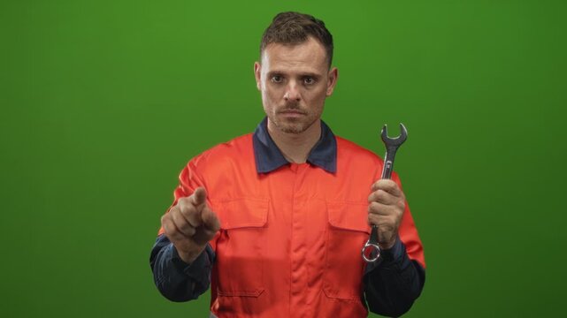 Man handyman pointing finger and holding wrench in studio wearing orange uniform and coverall while looking intently; repair focus determination.