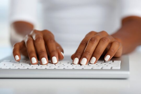 African female hands typing on a white keyboard with painted nails