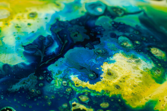 Colorful patterns show fluid movement in blue and green hues on a canvas