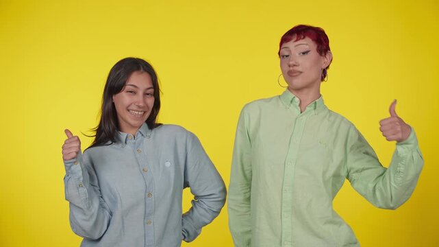 Two cheerful young women showing thumbs up gesture