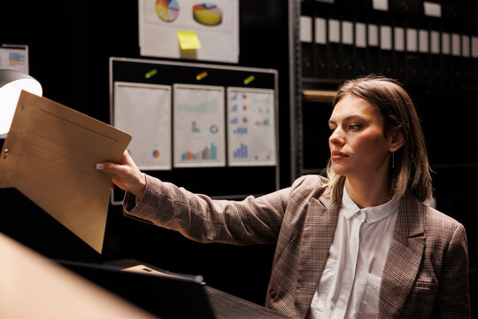 Private detective putting files on shelf after analyzing crime scene evidence searching for clues to solve case. Caucasian police officer working overtime in arhive room, checking criminology report