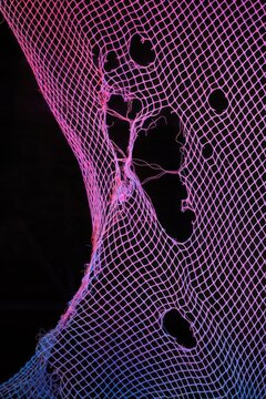 Vibrant pink and blue netting with holes against a dark background