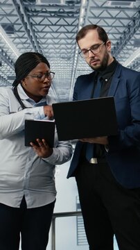 Vertical video Woman optimizes microchip smart factory workflow with coworker, using EDA software. Teamworking colleagues using simulation tool tracking semiconductor production circuit layout defects