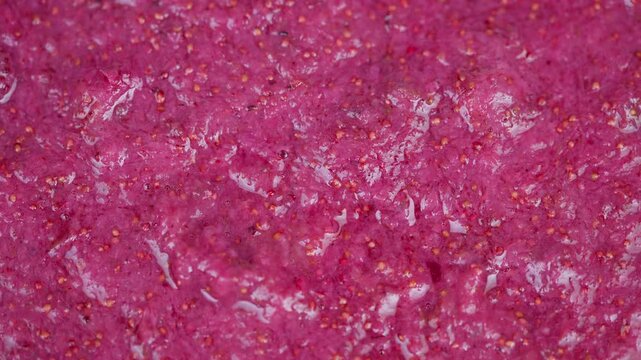 Vivid strawberry puree. Colorful fruit spread macro shot. Closeup of juicy strawberry mixture surface. Detailed macro view of textured strawberry puree surface with seeds