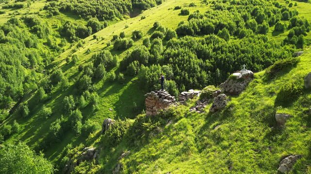 Epic green mountain valley vertical aerial orbit flyby ancient stone fortress ruins.
