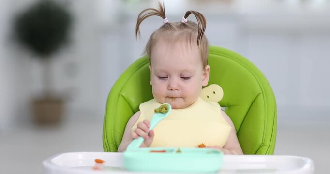 Cute little child eating baby food on feeding chair at home