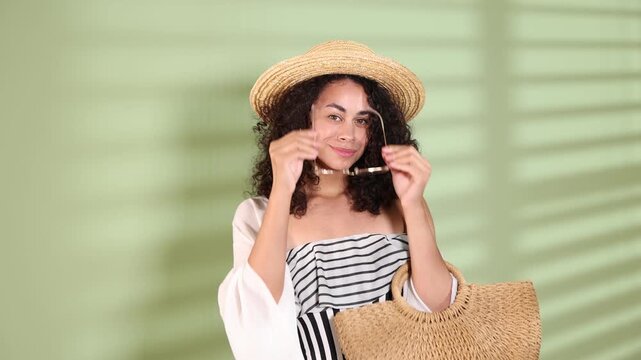 Woman with bag wearing stylish swimsuit, sunglasses and beach kimono near green wall indoors