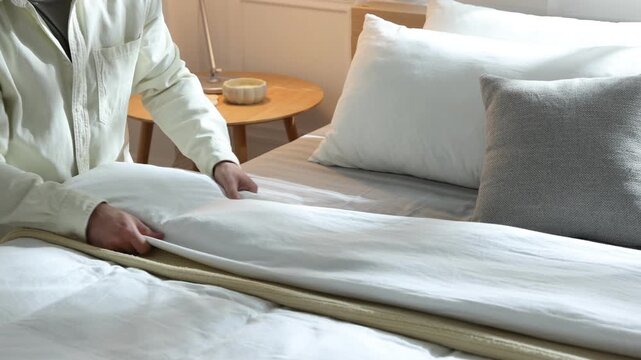 Man making bed near white wall at home, closeup