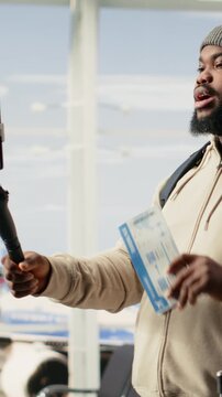 Vertical Video Black guy vlogger recording travel vlog on smartphone in airport lounge, using tripod for video content while waiting on departure. Gen Z influencer represents social media lifestyle