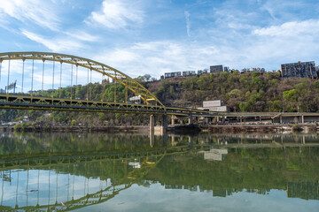 Fototapeta premium Fort Pitt Bridge Crosses Monongahela River in Pittsburgh With Clear Sky and Green Hillside in View During Daylight Hours