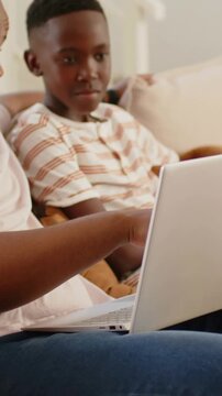 Vertical video: Tapping keys, father guiding son on beige couch at home, teaching on silver laptop
