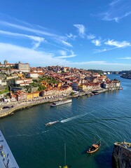 Obraz premium Scenic high-angle shot showcasing an old European city along a wide river under a bright blue sky dotted with wispy clouds. Boats dot the water